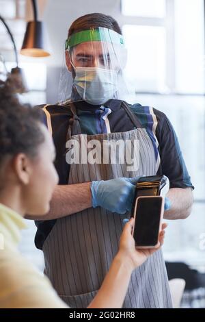 Vertikales Porträt eines Kellners mit Gesichtsschutz und Handschuhen Bedienung des Kunden im Café mit kovidierten Sicherheitsmaßnahmen Stockfoto