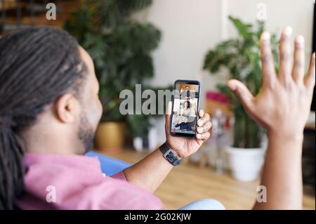 Gruppen-Videoanruf auf dem Smartphone. Ein afroamerikanischer Mann, der eine mobile App für die Videoverbindung mit verschiedenen Kollegen oder Freunden verwendet, winkt und grüßt Stockfoto