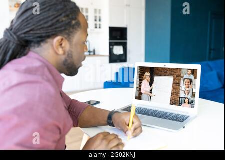 Intelligenter und konzentrierter afroamerikanischer Student mit Locks Frisur mit Laptop-Computer zum Lernen auf der Ferne, Notizen machen, Lehrer mit Whiteboard auf dem Bildschirm Stockfoto
