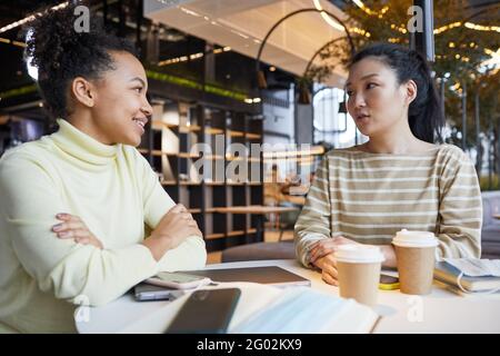 Portrait von zwei jungen Frauen, die beim Sitzen zusammen arbeiten Tisch im Café und lächelnd Stockfoto