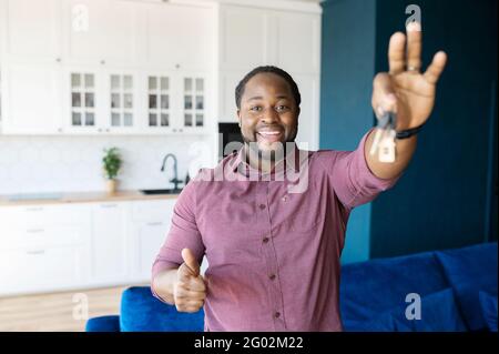 Eigenes Hotel. Positiv überglücklich afroamerikanischer Kerl zeigt Schlüssel aus neuem Haus und Daumen, kaufte eigene Wohnung, bekam Hypothek, verlegt oder umgezogen Stockfoto