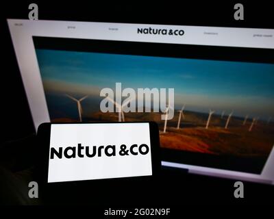 Person, die Mobiltelefon mit dem Logo des brasilianischen Körperpflegeunternehmens Natura Co Holding S.A. auf dem Bildschirm vor der Webseite hält. Konzentrieren Sie sich auf die Telefonanzeige. Stockfoto