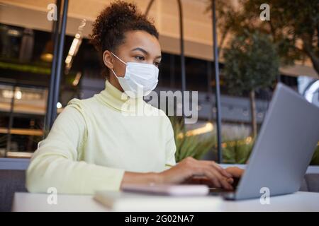 Low-Winkel-Porträt der asiatischen jungen Frau trägt Maske und Mit Laptop während der Arbeit am Tisch im Café Stockfoto