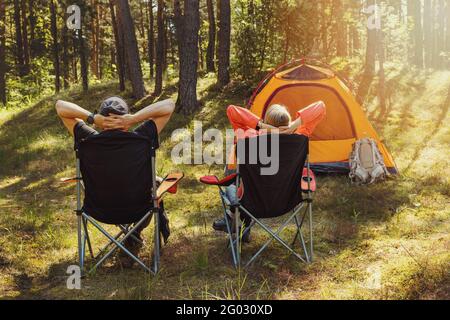 Menschen entspannen in Campingstühlen auf Waldcampingplatz und genießen Die Natur Stockfoto