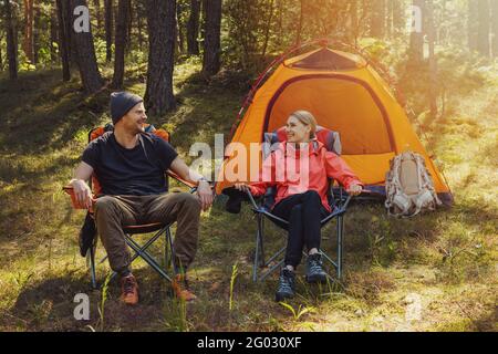 Glückliches Paar, das sich nach der Wanderung in Campingstühlen auf dem Campingplatz entspannt Im Wald Stockfoto