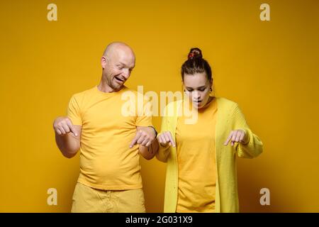 Mann und Frau blicken schockiert nach unten und zeigen mit dem Zeigefinger auf etwas. Gelber Hintergrund. Stockfoto