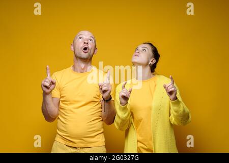 Überraschte Männer und Frauen zeigen ihre Zeigefinger nach oben und starren ungläubig. Gelber Hintergrund. Stockfoto