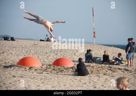 Junge Leute, die am Strand einen Übungsball spielen, der im Sand vergraben ist Stockfoto