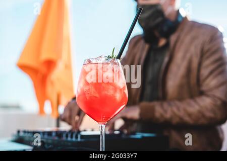 Nahaufnahme eines besonderen Cocktails bei einer Strandparty - DJ spielt Musik an der Cocktailbar im Freien mit Sicherheitsgesicht Maske für Coronavirus-Ausbruch - Entertain Stockfoto