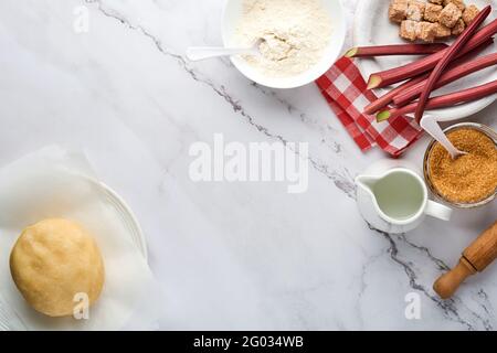 Teigkugel und Zutaten Mehl, Wasser, Butter, Zucker und Rhabarber zum Backen auf weißem Marmorboden mit Stauben von Mehl. Rezept Schritt für Schritt Stockfoto