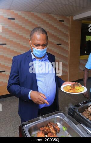 KAMPALA, UGANDA - 27. Mai 2021: Ein afroamerikanischer sanfter Mann, der Essen bekommt und auf alles zeigt, was er will, ohne seine Maske zu entfernen, um h zu verhindern Stockfoto