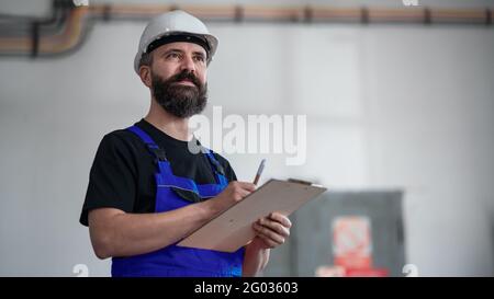 Low-Angle-Ansicht des Arbeiters mit Helm in Innenräumen in der Fabrik halten Zwischenablage. Stockfoto