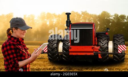 Eine Farmerin mit digitalem Tablet steuert einen autonomen Traktor an Eine intelligente Farm Stockfoto