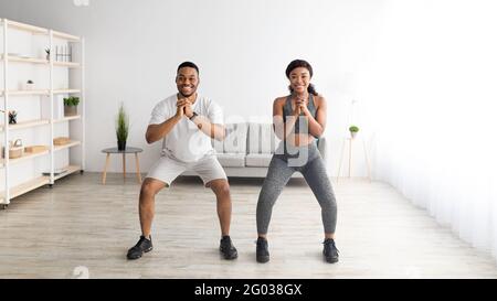 Inländisches Krafttraining. Motivierte schwarze Dame und ihr männlicher Partner hocken zusammen zu Hause, Bannerdesign Stockfoto