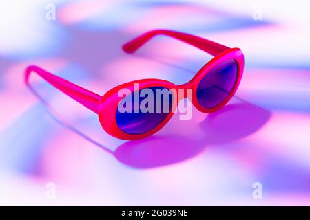 Rote Sonnenbrille in Monstera Blatt Schatten auf einem Hintergrund von Sommer- oder Neonfarben Stockfoto