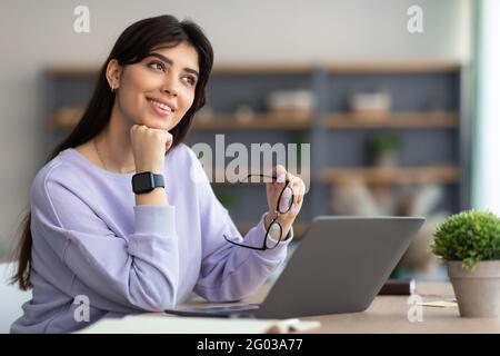Porträt einer lächelnden jungen Frau, die am Schreibtisch sitzt und denkt Stockfoto