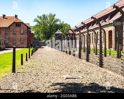 Oświęcim, Polen - Juni 05, 2019: elektrischen Zaun mit Stacheldraht und Ziegel Gefängnis Gebäuden im Konzentrationslager Auschwitz-Birkenau in Oświęcim, Stockfoto
