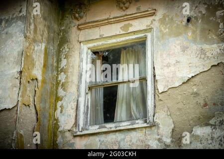 Ein beschädigtes Schiebefenster mit Vorhangsresten in einem verlassenTeil zerstörten Haus Stockfoto