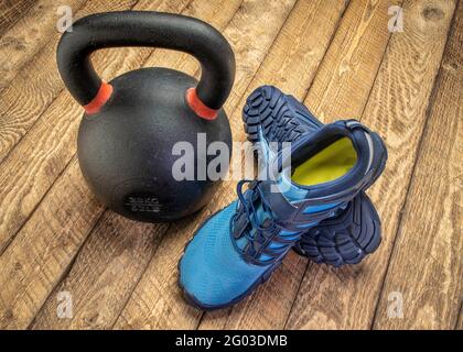 Barfuß-Cross-Trainingsschuhe auf rustikalem Holzhintergrund mit schwerer eiserner Kettlebell, Fitnesskonzept Stockfoto