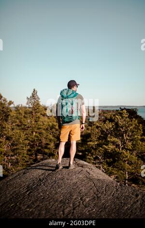 Die ganze Länge des reifen Mannes stehend mit Rucksack auf dem Felsen während des sonnigen Tages Stockfoto