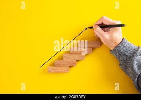 Man Hand Zeichnung einen nach oben zeigenden Pfeil auf der wachsenden Grafik aus Holzblock. Auf gelbem Hintergrund Stockfoto