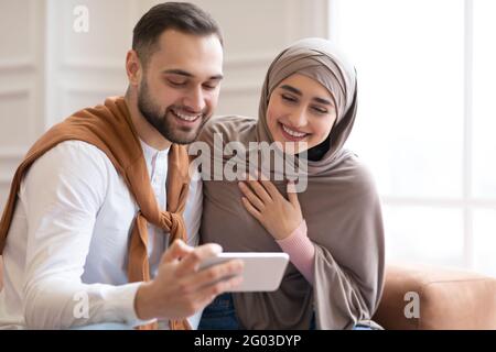 Fröhliches Muslimisches Paar Mit Smartphone Gemeinsam Spaß Zu Hause Haben Stockfoto