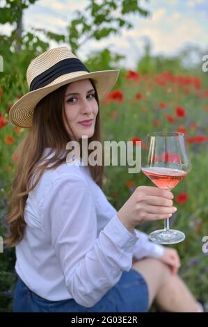 Junge Frau mit Rosenwein im Glas auf Mohn Stockfoto