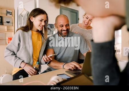 Lächelnde Frau und Tochter, die den Mann beim Online-Shopping zu Hause betrachten Stockfoto