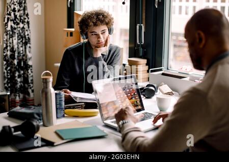 Teenager, der den männlichen Unternehmer beim Arbeiten ansieht, während er am Schreibtisch sitzt Stockfoto