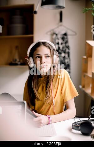 Mädchen, das Kopfhörer trägt, sitzt am Schreibtisch und schaut weg Stockfoto