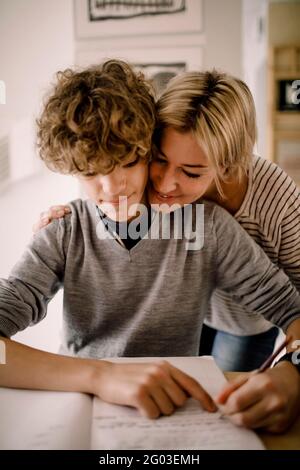 Lächelnde Mutter umarmt Sohn bei Hausaufgaben Stockfoto