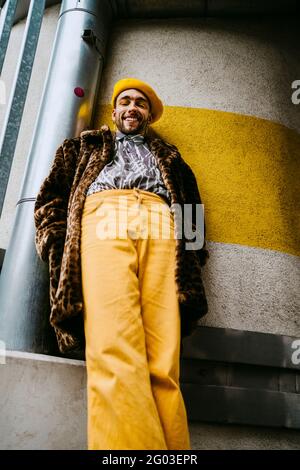 Lächelnder junger Mann mit Händen in Taschen, die gegen die Wand stehen Stockfoto