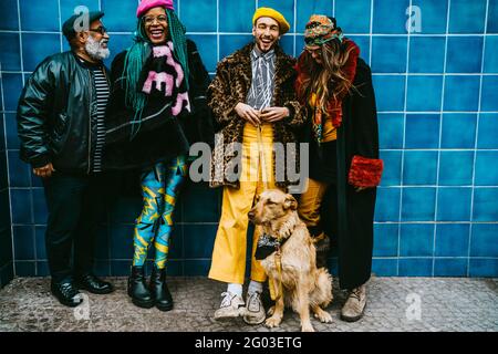 Volle Länge von glücklichen männlichen und weiblichen Freunden mit Hund gegen blaue Wand Stockfoto