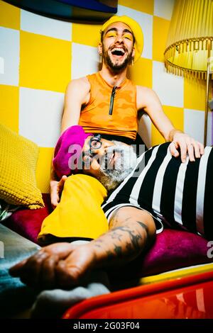 Lächelnder älterer Mann, der auf dem Schoß eines männlichen Freundes im Wohnzimmer liegt Stockfoto