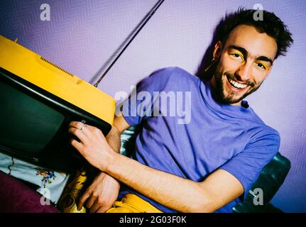 Porträt eines fröhlichen jungen Mannes, der mit einem altmodischen Fernseher in der Wohnung sitzt Stockfoto