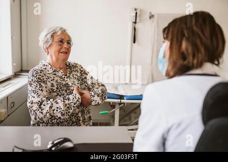 Leitende weibliche Patientin, die während der COVID-19-Konsultation mit einer medizinischen Fachkraft diskutiert Stockfoto