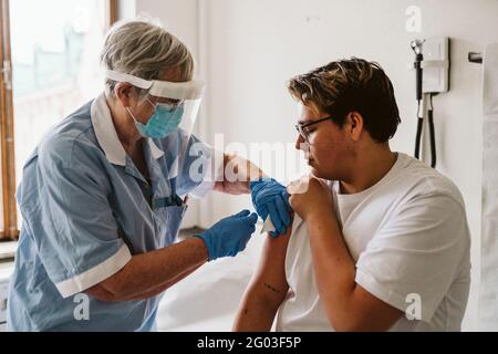 Leitende Angestellte im Gesundheitswesen, die während des COVID-19 jungen männlichen Patienten Impfstoffe verabreichten Stockfoto