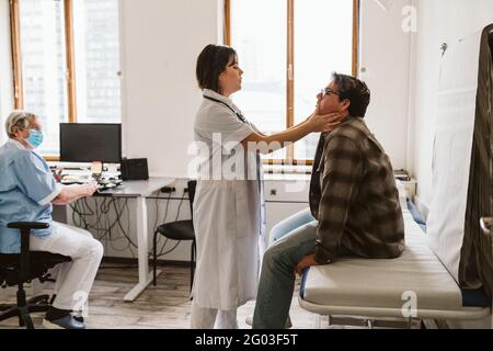 Leitende Krankenschwester, die den Arzt anschaut, der den Puls eines männlichen Patienten in der medizinischen Klinik überprüft Stockfoto