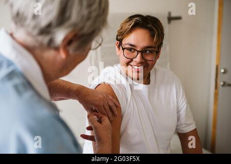 Lächelnder männlicher Patient, der eine leitende Ärztin ansieht, die in der medizinischen Klinik einen Impfstoff verabreicht Stockfoto