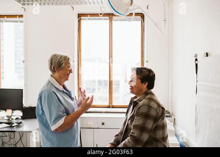 Leitende Ärztin gestikuliert, während sie mit jungen männlichen Patienten in der medizinischen Klinik diskutiert Stockfoto