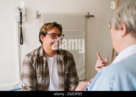 Lächelnder junger männlicher Patient, der eine leitende Ärztin in der medizinischen Klinik anschaut Stockfoto