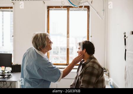 Leitende Angestellte im Gesundheitswesen untersucht den Hals eines männlichen Patienten in einer medizinischen Klinik Stockfoto