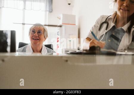 Ärztin, die ein Rezept von einer Krankenschwester schreibt, die wegschaut Stockfoto