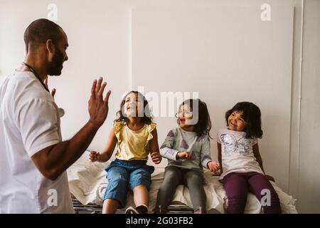 Glückliche Mädchen sitzen auf Untersuchungstisch Blick auf männlichen Arzt gestikulieren in der medizinischen Klinik Stockfoto
