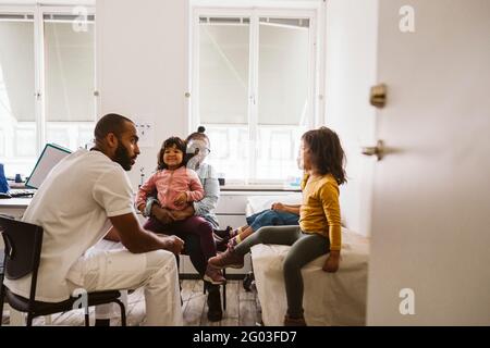 Lächelnde Mutter und Tochter, die einen männlichen Arzt aufsuchen und Mädchen in der medizinischen Klinik beraten Stockfoto