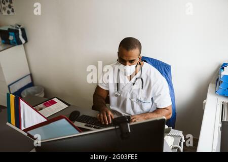 Männlicher Mitarbeiter im Gesundheitswesen trägt Gesichtsmaske mit Computer in der medizinischen Klinik Stockfoto