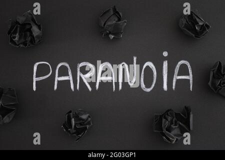 Das Wort Paranoia auf einem schwarzen Hintergrund mit schwarzen zerknitterten Papierkugeln um es herum. Nahaufnahme. Stockfoto