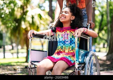 Kleines Mädchen im Rollstuhl im Park mit ihrer Mutter. Stockfoto