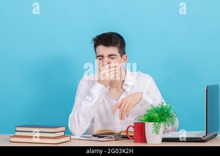 Gelangweilter oder müder Student, der an der Rezeption mit Büchern gähnt Und Computer Stockfoto