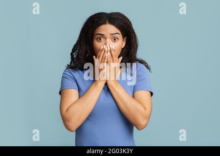 Oh nein Schockiert und verängstigt, bedeckte eine afroamerikanische Frau ihren Mund mit Handflächen und stand über blauem Studiohintergrund Stockfoto
